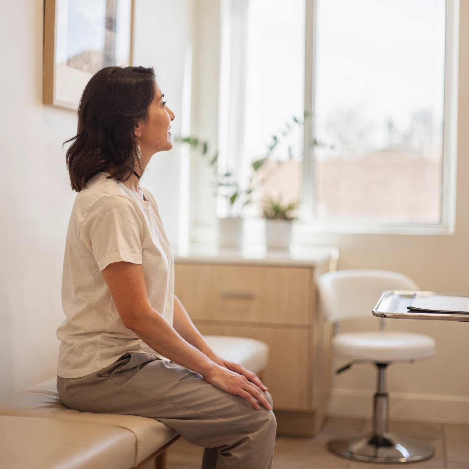 Patient sitting on examination table in bright clinic room with large windows